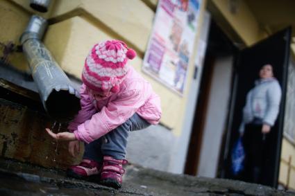 Маленькая девочка полощет ручки в воде с водосточной трубы. Екатеринбург