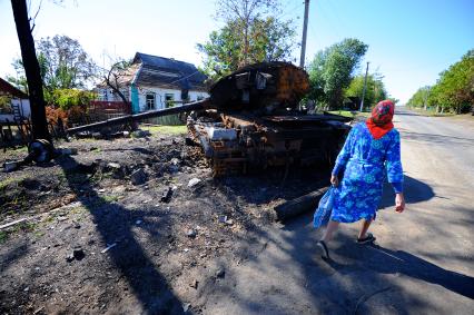 Украина. Донецкая область. с.Степановка. Местная жительница идет по дороге мимо сгоревшей военной техники.