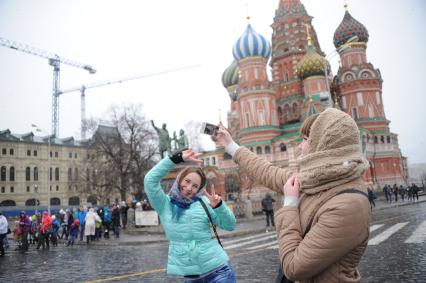 Девушки фотографируются на фоне храма Василия Блаженного в Москве.