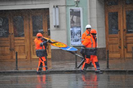 Снегопад в Москве.  Рабочие несут дорожные знаки по Тверской улице.