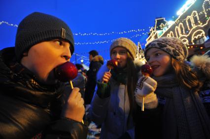 Москва. Подростки едят гализрованные яблоки на территории Рождественской ГУМ-Ярмарки на Красной площади.