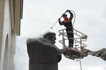 Сотрудник коммунальной службы моет памятник Петру Добрынину  перед внешним вестибюлем станции метро `Добрынинская` в Москве.