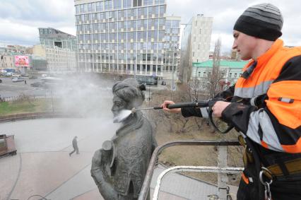 Сотрудник коммунальной службы моет памятник Алишеру Навои  в сквере на Серпуховской площади  в Москве.