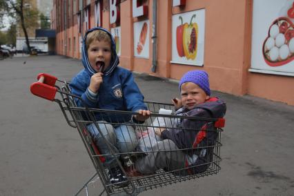 Москва. Дети сидят в магазинной тележке.