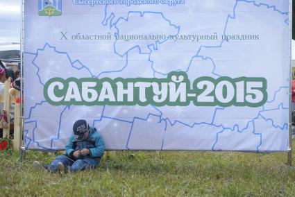 Ребенок сидит у плаката с надписью \"Сабантуй-2015\", во время празднования Сабантуя. село Кадниово. Свердловская область