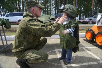 Военнослужащий одевает на ребенка бронежилет и армейскую каску с защитными очками, перед началом военно-спортивной игры \"Гонка героев\" на полигоне 32-го военного городка. Екатеринбург