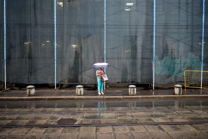 Проливной дождь в Москве. Женщина под зонтом стоит на тротуаре у трамвайных путей.