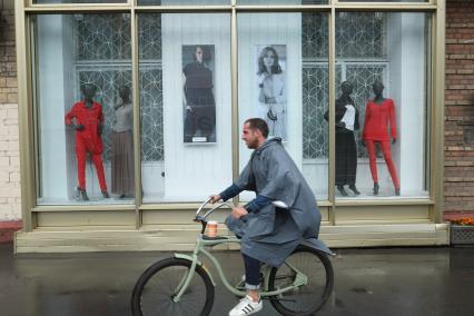 Проливной дождь в Москве. Мужчина в дождевике едет на велосипеде.