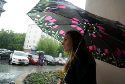 Девушка под зонтом пережидает дождь стоя в арке дома. Екатеринбург
