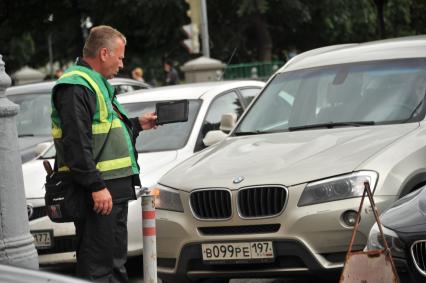 Москва. Контролер `Московского паркинга` снимает на планшет номера автомобилей, стоящих в зоне платной парковки, с целью проверки оплаты места.