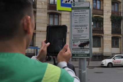 Москва. Контролер `Московского паркинга` снимает на портативный комплекс фото-видеофиксации замазанный номер парковки на информационном стенде.