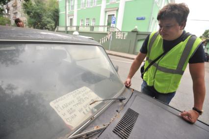 Москва. Контролер `Московского паркинга` стоит у грязного автомобиля с надписью под стеклом `Машину не трогать`.