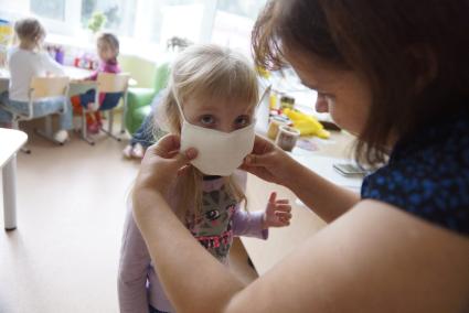 Воспитатель помогает ребенку одеть ватно-марлевую повязку, во время учебной эвакуации из детсого сада при пожаре. Екатеринбург