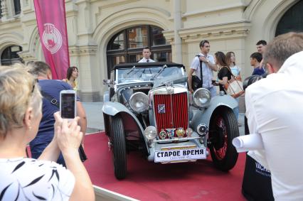 Москва. Женщина фотографирует на мобильный телефон автомобиль MG во время `ГУМ-Авторалли-2015` с участием ретро-автомобилей в Ветошном переулке.