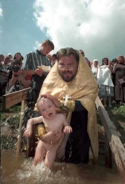 Священник крестит ребенка в воде.