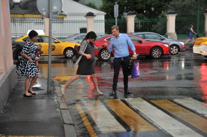 Ливень в Москве. Мужчина помогает беременной девушки перейти дорогу.