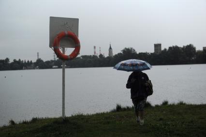 Ливень в Москве. Женщина под зонтом идет мимо озера Белое.