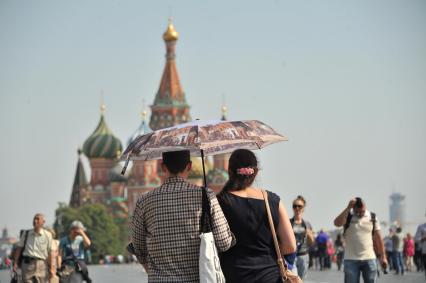 Москва. Пара стоит под зонтом на Красной площади и смотрит на Собор Василия Блаженного.