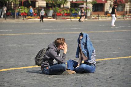 Москва. Парень с девушкой разговаривают, сидя на брусчатке на Красной площади.