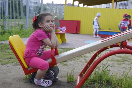 Девочка одно сидит на качели, на площадке детского сада во время прогулки в. Екатеринбург
