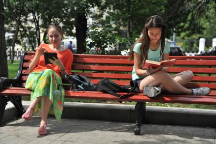 Москва.  Девушки читают книги, сидя на скамейке в парке.