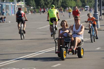 Москва.  Мужчина с девушкой катаются на веломобиле в Парке Горького.