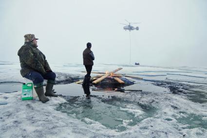 Полярники у костра из остатков стройматериалов и мусора, наблюдают как вертолет Ка-32 МЧС России перевозит аппаратуру и имущество с сезонной дрейфующей станции \"Северный полюс 2015\" из Арктики, на ледокол \"Капитан Драницын\" перед эвакуацией на большую землю. Северный полюс. Северный ледовитый океан