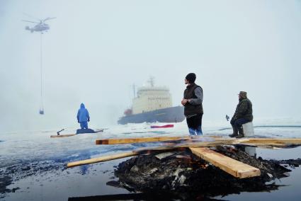 Полярники у костра из остатков стройматериалов и мусора, наблюдают как вертолет Ка-32 МЧС России перевозит аппаратуру и имущество с сезонной дрейфующей станции \"Северный полюс 2015\" из Арктики, на ледокол \"Капитан Драницын\" перед эвакуацией на большую землю. Северный полюс. Северный ледовитый океан