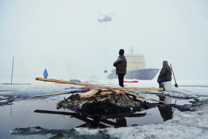 Полярники у костра из остатков стройматериалов и мусора, наблюдают как вертолет Ка-32 МЧС России перевозит аппаратуру и имущество с сезонной дрейфующей станции \"Северный полюс 2015\" из Арктики, на ледокол \"Капитан Драницын\" перед эвакуацией на большую землю. Северный полюс. Северный ледовитый океан