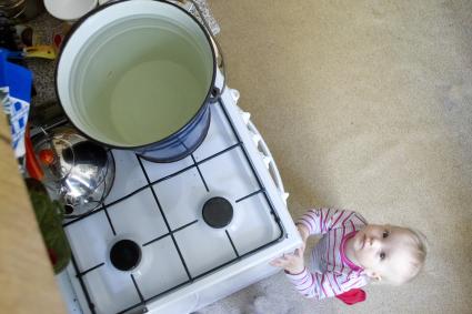 Маленький ребенок у газовой плиты, на которой греется вода в ведре для купания. Екатеринбург