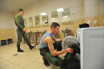 Военнослужащий складывает форма у стиральную машину.