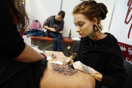 Екатеринбург. Мастер набивает татуировку участнице фестиваля искусства татуировки `Ural tattoo fest 2015`.