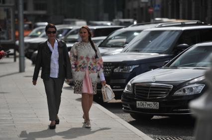 Москва. Женщины идут мимо припаркованных автомобилей.