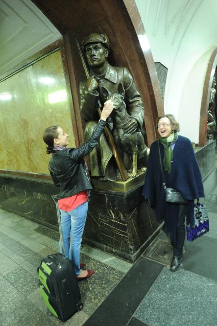 Москва.  Девушка гладит нос собаки скульптуры `Пограничник с собакой` на станции метро `Площадь Революции`.