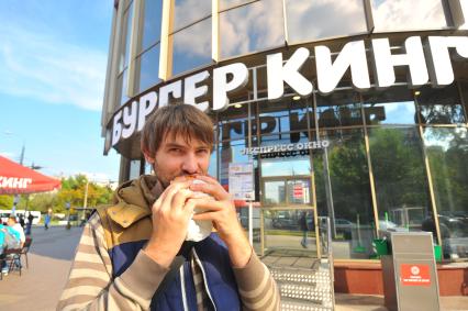 Москва. Мужчина ест гамбургер у ресторана быстрого питания `Бургер Кинг`.