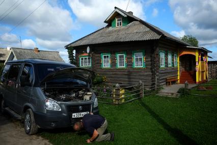 Архангельская область. г.Каргополь. Мужчина ремонтирует автомобиль у деревянного дома.