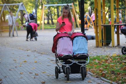 Москва. `Бабье лето`. Женщина гуляет с детской коляской и смотрит в мобильный телефон.