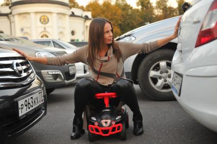 Москва. Девушка на детской машинке на парковке.