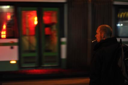 Москва. Мужчина курит у автобусной остановки.
