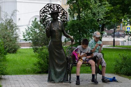 Самара. Дети смотрят в мобильные телефоны, сидя на скамейке скульптуры `Дама с ракеткой`.