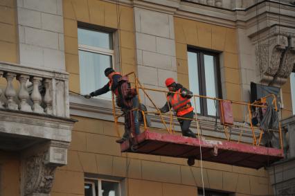 Москва.  Рабочие ремонтируют фасад здания.