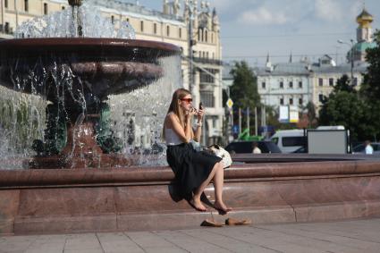 Москва. Девушка поправляет макияж, сидя у фонтана на Тетральной площади.