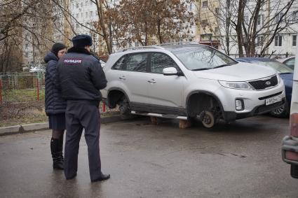Тула. Женщина и сотрудник полиции стоят у машины со снятыми грабителями колесами.
