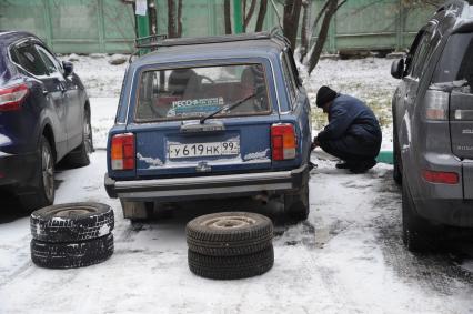 Москва.  Первый снег. Мужчина меняет колеса автомобиля.