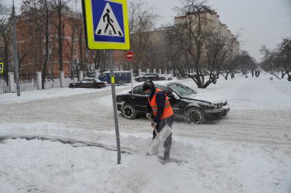Москва. Гастарбайтер убирает снег на улице.