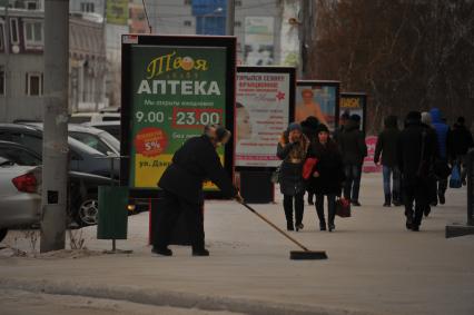 Республика Саха (Якутия), Якутск. Мужчина подметает щеткой тротуар.