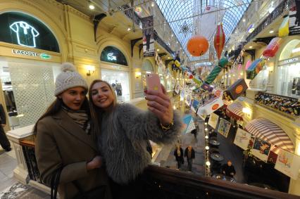 Москва. Девушки делают селфи на фоне новогоднего украшения в ГУМе.