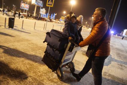 Екатеринбург. Аэропорт Кольцово. Мужчина везет детей, сидящих верхом на чемоданах.