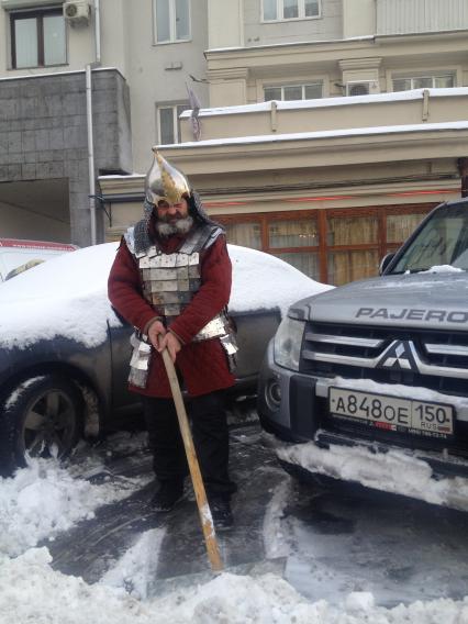 Москва. Мужчина в костюме русского былинного богатыря очищает снег около машины.