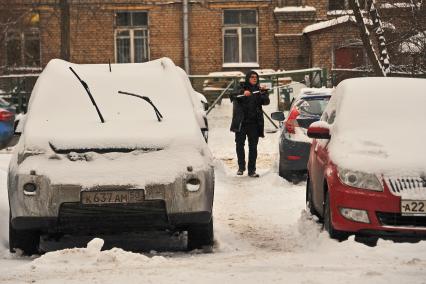 Последствия метели в Москве. Водитель счищает снег с машины.